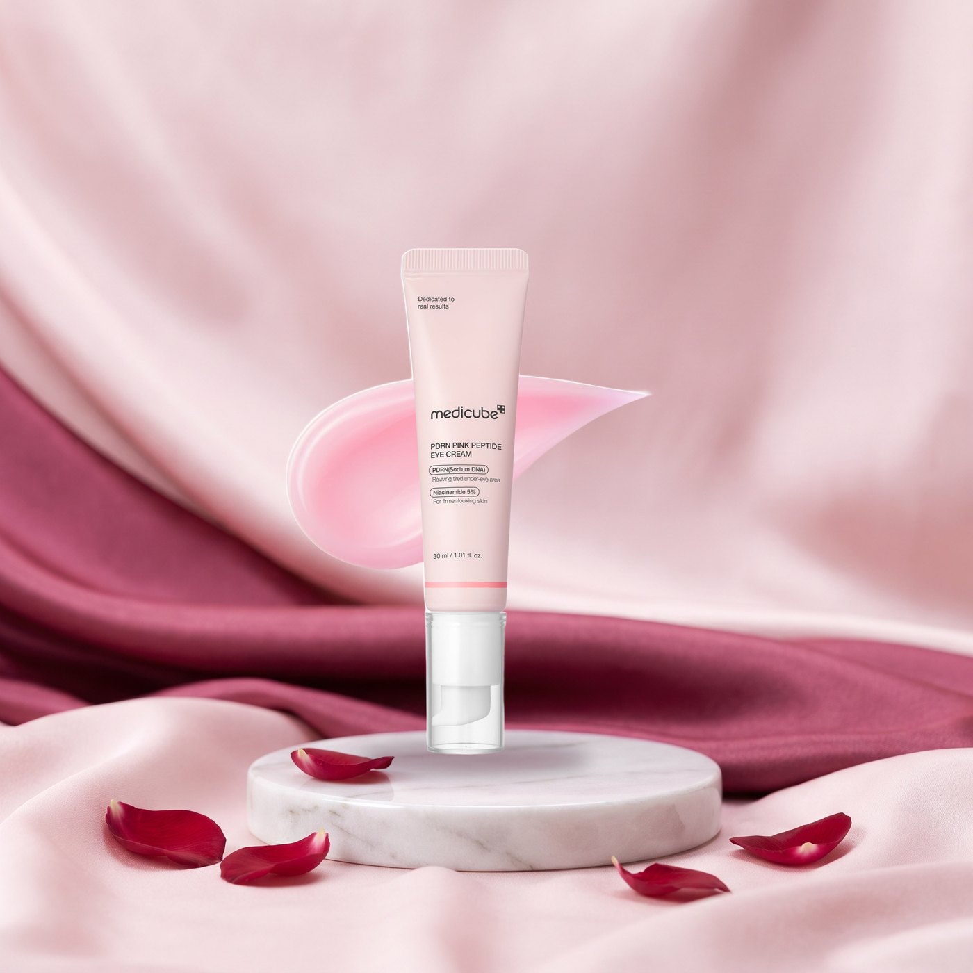 Medicube PDRN Pink Peptide Eye Cream sobre pedestal de marmol con seda rosa